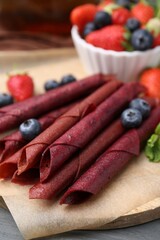 Tasty fruit leather rolls, strawberries, blueberries and mint on grey wooden table, closeup