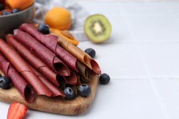 Tasty candied leather rolls, fruits and berries on white tiled table, closeup. Space for text