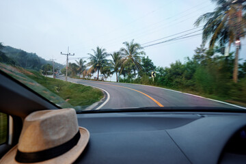 Scenic Coastal Road View Through Car Windshield With Straw Hat on Dashboard..