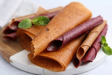 Delicious fruit leather rolls and mint on light table, closeup