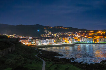 Stunning night view of Baiona Bay, Spain, illuminated by city lights and moonlight, creating a...