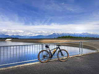 A mountain bike rests against a railing by a serene reservoir, showcasing a beautiful landscape of mountains under a clear sky, perfect for outdoor adventures and cycling