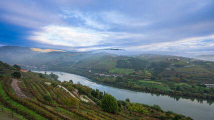 Fototapeta premium Panoramic view from a hilltop hotel balcony overlooking the serene Douro River winding through picturesque vineyards near Lamego, Portugal.