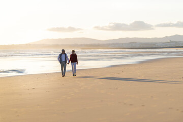 Senior couple walking on the beach at sunset