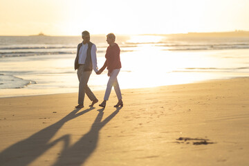 Senior couple holding hands walking on beach at sunset