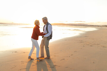 Happy senior couple dancing barefoot on the beach at sunset