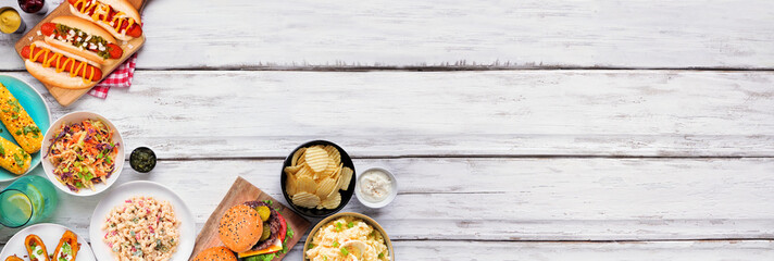 Summer food table scene with hot dogs, hamburger and sides. Top view corner border over a white wood banner background. Copy space.