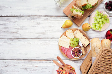 Summer picnic food side border. Top view over a white wood background. Picnic basket, fruit, salad, sandwiches and snacks. Copy space.