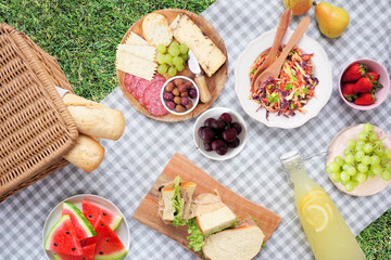 Summer picnic food scene. Top view with blanket over a green lawn background. Picnic basket, fruit, salad, sandwiches and snacks.