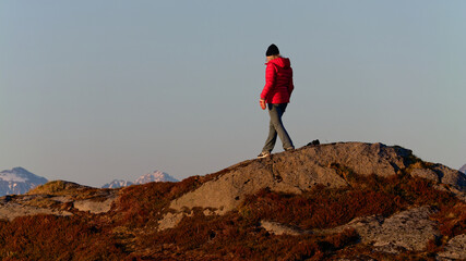 Woman in jeans, red jacket and black hat  in the mountains on a sunny spring day. Lofoten, Northern...