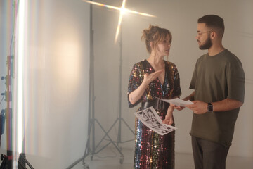 Waist up portrait of young woman talking to director while holding concept art drafts and discussing video scene backstage in studio