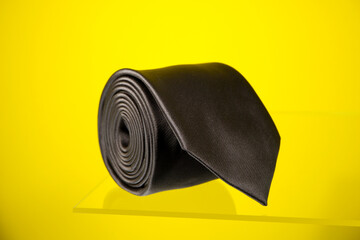 A black tie rolled on yellow background closeup view 