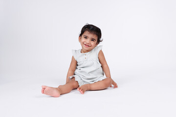 Cute happy little baby girl sitting and playing on floor with happy facial expression wearing white dress isolated on white background