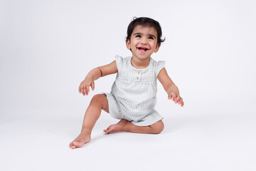 Cute happy excited little baby girl trying to standup with happy facial expression wearing white dress isolated on white background