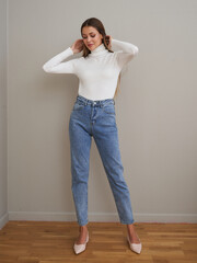 Young brunette model showcases slim style in fitted turtleneck and high-waisted jeans
