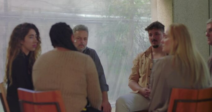 Therapy group seated in supportive circle, individuals listening attentively to emotional testimony during group counseling session