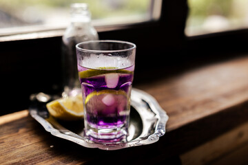 purple cocktail with lime slices and ice, alongside a soda bottle on a silver tray. Perfect for cocktail menus, food styling, or luxury beverage ads with its vibrant hue.