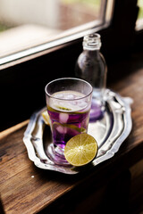 Chilled purple cocktail with lime slices and ice, paired with a soda bottle on a silver tray. Perfect for restaurant marketing, beverage campaigns, or lifestyle blogs.