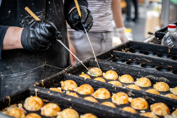 Japanese street vendor cooking takoyaki using traditional round molds at an outdoor food market....