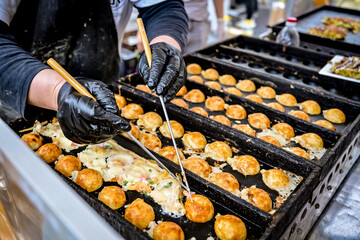 Japanese street vendor cooking takoyaki using traditional round molds at an outdoor food market....