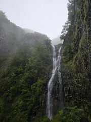 Tall waterfall cascading through misty cliffs on Madeira&rsquo;s Levada das 25 Fontes trail. Rain-soaked rocks and lush vegetation create a wild, serene atmosphere.