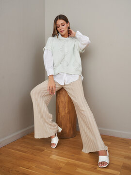 Stylish young woman in white knitted top and beige pants poses indoors
