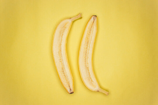 Top view photo of one cut in half raw banana on the yellow background