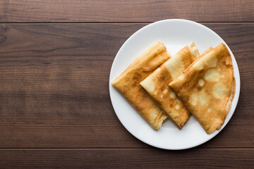 Top view photo of crepes, thin pancakes, British pancakes on the white plate over wooden background with copy space.