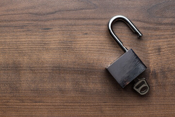 Top view photo of opened padlock with key inside on the brown wooden table background with copy...