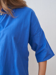 A woman in a vibrant blue shirt with short sleeves, partially cropped, revealing a hint of her left...