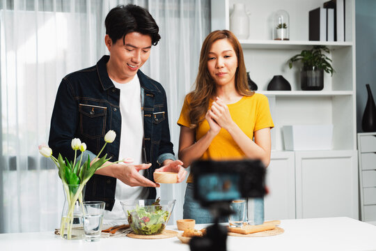 Cooking show on live streaming with two chef influencers teaching mixed salad, preparing ingredients with dressing for easy special menu served with bun bread on table recorded by camera. Infobahn.