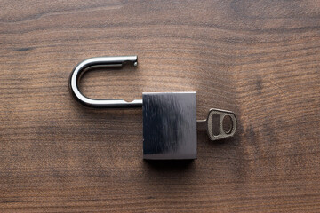 Top view photo of opened padlock with key inside on the brown wooden table background central...