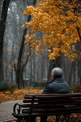 Fototapeta premium Man sitting on park bench in autumn looking at fall foliage