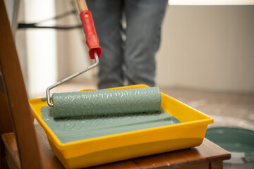 Painter dipping a patterned paint roller into a tray filled with vibrant green paint, getting ready...