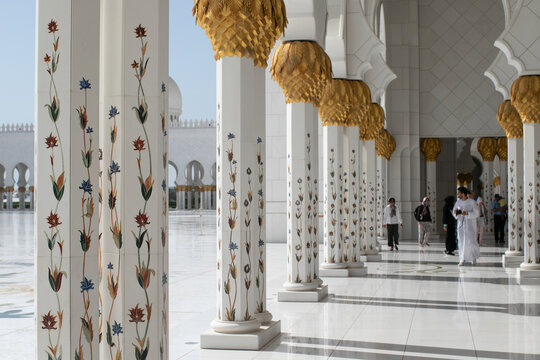 White domes and floral columns of Sheikh Zayed Grand Mosque with tourists exploring the courtyard