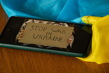 Poster with the text Stop War in Ukraine in the hands of a girl on the screen of a smartphone lying...