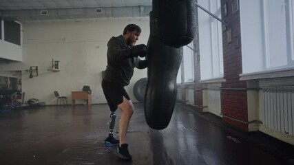 Focused man with prosthetic leg practices boxing punches on bag - Powered by Adobe