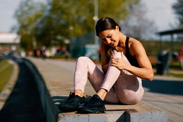 Young sportswoman suffering from knee pain after a workout injury in a park