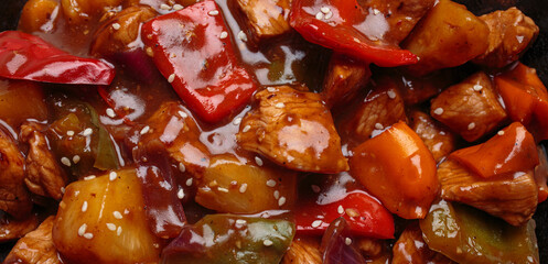 Sweet and sour pork with bell peppers and pineapple is cooking in a wok, sprinkled with sesame...