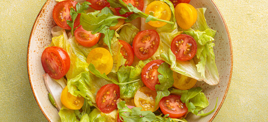 Fresh and vibrant mixed salad with crisp lettuce, juicy red and yellow cherry tomatoes and arugula. Served in a bowl with cutlery on the side. Vitamins and healthy eating habits