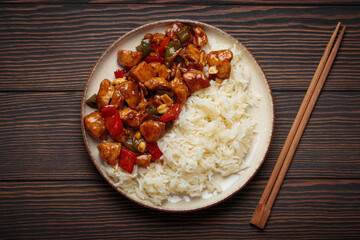 Steaming Chinese kung pao chicken with rice, veggies, and peanuts in spicy sauce. Top view on wooden background. Perfect for lunch or dinner