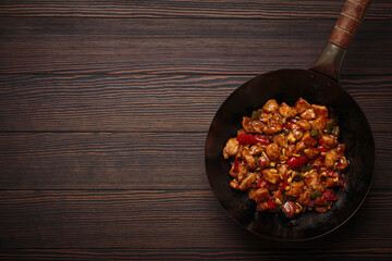 Wok pan containing Chinese kung pao chicken, a stir fried dish made with chicken, peanuts, vegetables and pepper, served on a wooden table, copy space