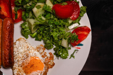 Breakfast plate featuring fried egg, sausages, fresh salad, and vibrant vegetables on a wooden table