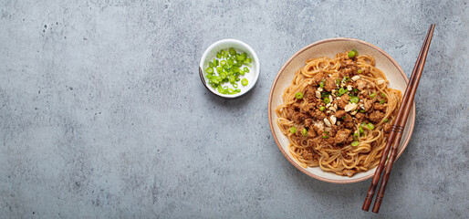 Dan dan noodles are being served with chopsticks and green onions in a bowl, showcasing the...