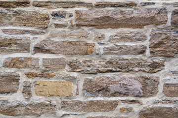 Close-up of a rustic stone wall with rough brown blocks and light mortar. Ideal background texture for architectural, construction, or design-related projects.