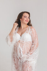 Beautiful pregnant young girl in a white lace long dress on a white background in a photo studio....