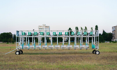 Starting gate positioned on a grassy field near residential buildings during the early evening hours