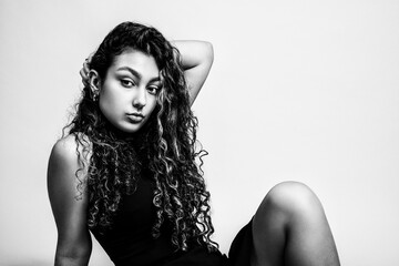 Black and white portrait of a beautiful teenage girl in a black dress. Sitting pose.
