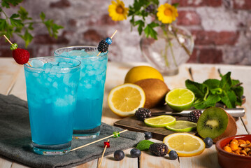 Glasses of ice and a blue exotic fruit soda, made from fruit juice, next to a cutting board with pieces of various exotic fruits. Close-up.