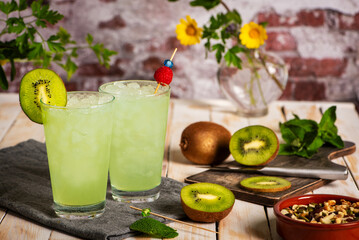 Glasses of ice with kiwi soda made from fruit juice, next to a cutting board with kiwi slices. Close-up.